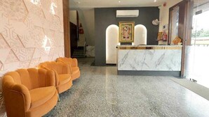 A reception area with a marble counter, a framed picture above it, and a row of orange chairs. - Hotel Shrinath Palace (Mathura)