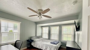 A bedroom with a bed, a desk, and a ceiling fan.