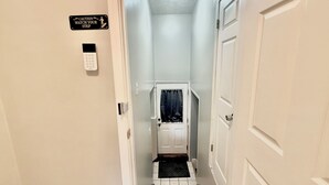 A narrow hallway with a door at the end, a caution sign, and a keypad lock.