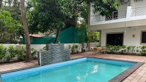 Piscina rectangular con pared de piedra y una pequeña cascada, rodeada por un patio empinado y follaje.