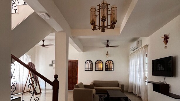 Amplia sala de estar con escalera, candelabro, conjunto de sofá, mesa de centro y televisor de pantalla plana montado en la pared.