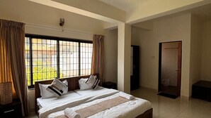 Un dormitorio amplio con una cama grande, ventilador de techo y vistas a través de una ventana con cortinas.