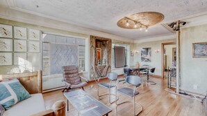 A spacious living room with a wooden floor, a large window, and a modern ceiling light fixture. - Historic Artist Home-Walk to SXSW+6th St+UT (Austin)