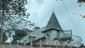 Un mur de pierre avec un portail en métal, un bâtiment doté d’un toit conique et une petite fenêtre.