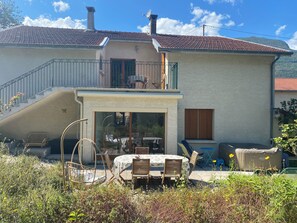 Ein zweistöckiges Haus mit Balkon, einem Essbereich mit Gartenmöbeln und einem Garten.