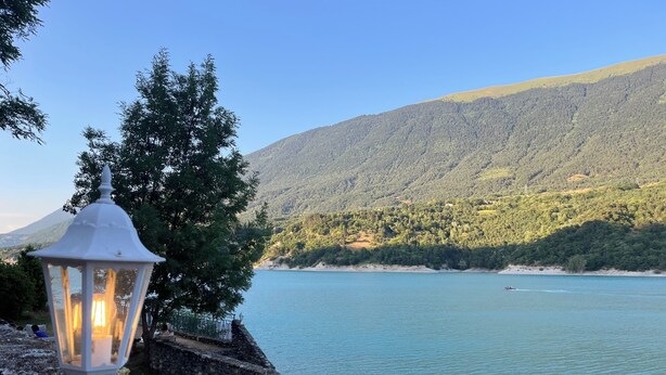 Une lanterne blanche, posée sur une corniche de pierre, surplombe un lac paisible, avec une montagne en arrière-plan.