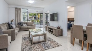 A modern living room with a sofa, coffee table, TV, and a dining area with chairs.