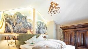 A bedroom with a wooden bed, a large painting of mountains, a wooden cabinet, and a unique ceiling light fixture. - Holiday home with a sauna near three ski resorts (Pfunds)
