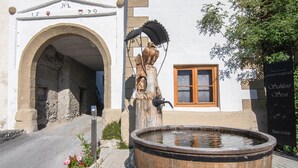 A building with a large wooden barrel fountain, an arched entrance, and a window with a wooden frame. - Holiday home with a sauna near three ski resorts (Pfunds)