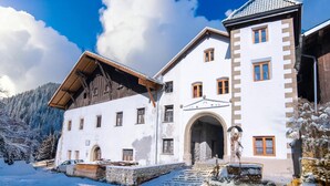 A large, white building with a stone entrance and wooden beams, surrounded by snow-covered trees and a clear sky. - Holiday home with a sauna near three ski resorts (Pfunds)