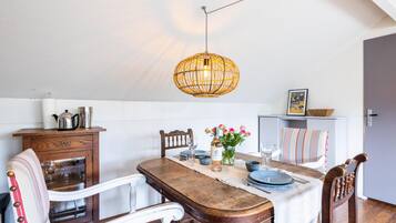 Un coin repas comprenant une table en bois, des chaises, un luminaire suspendu et un meuble contenant des ustensiles de cuisine.