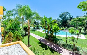 A well-maintained garden with a pathway leading to a pool area, surrounded by various tropical plants and trees.