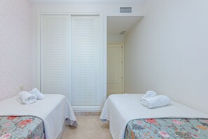 A bedroom with two beds, each with a floral bedspread and a white quilt. There is a white closet with sliding doors and a small vent above it.