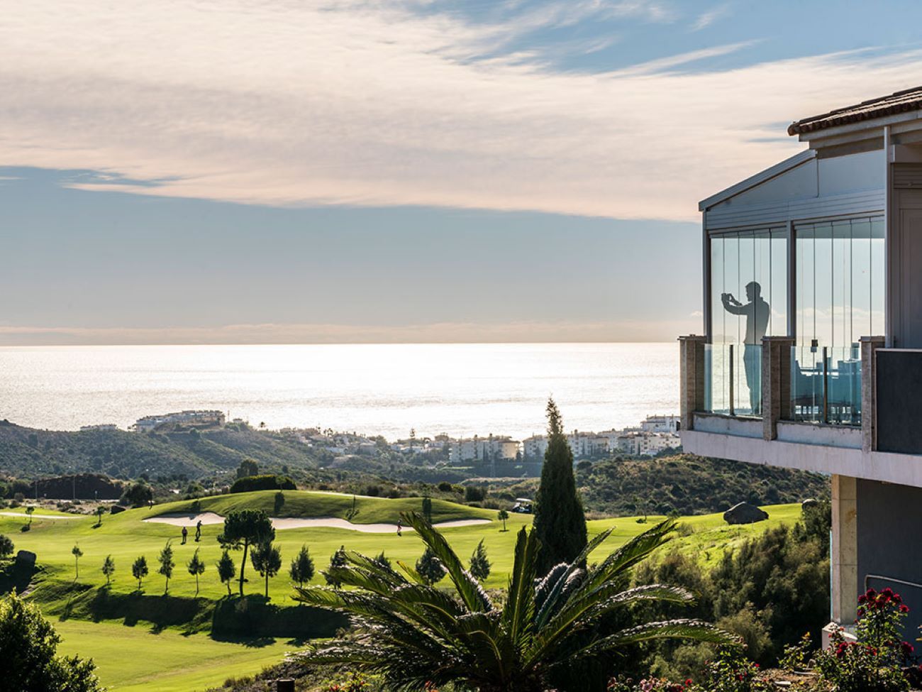 A modern building with large glass windows overlooking a golf course and the ocean.