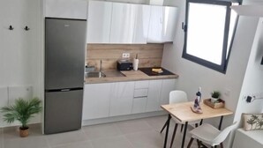 Una cocina compacta con armarios blancos, un refrigerador de acero inoxidable, una encimera de madera y una pequeña mesa de comedor con sillas.