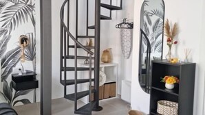 Un interior moderno con una escalera espiral, una consola blanca y un espejo con diseño de hoja de palma.