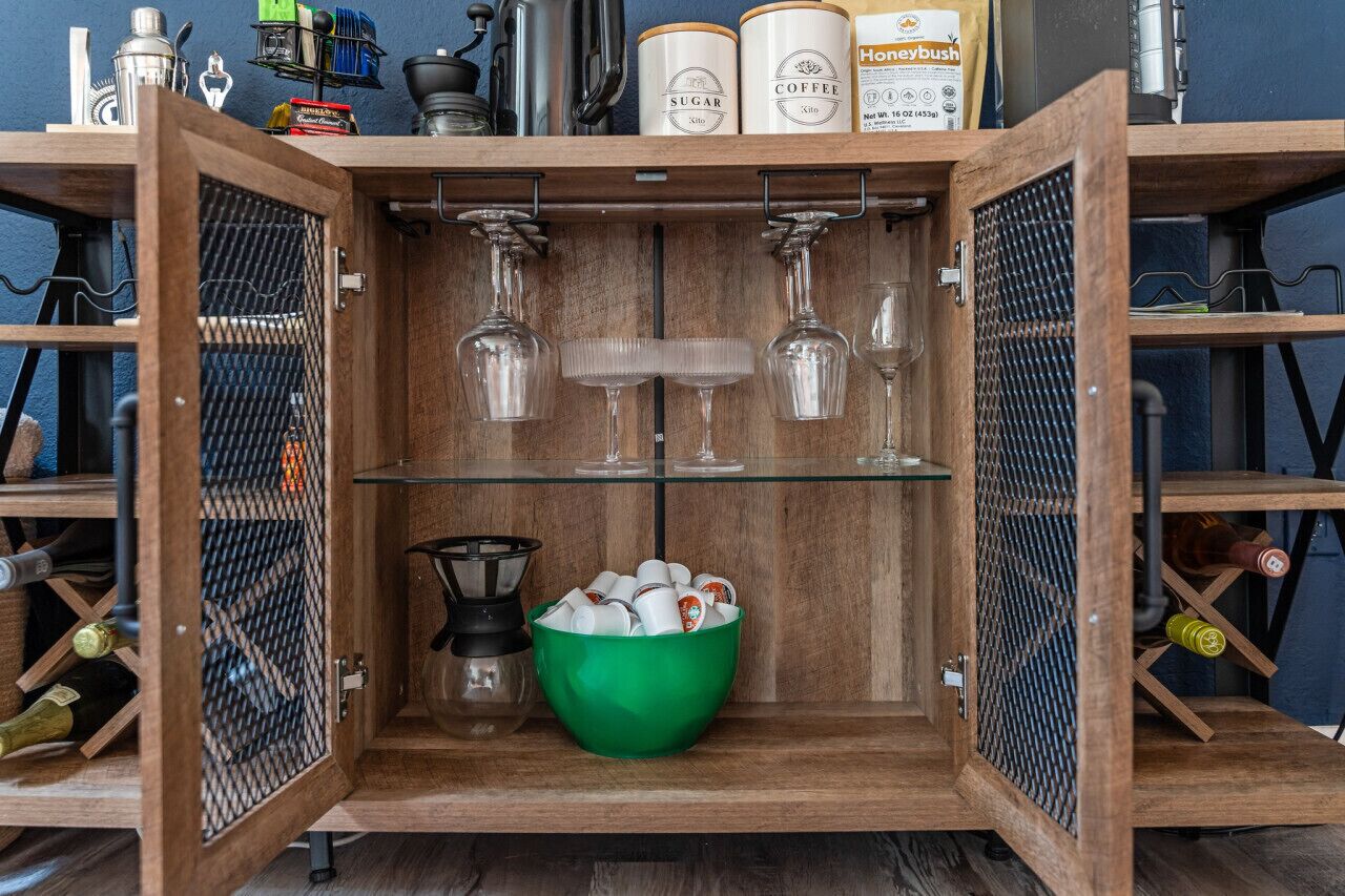 Stylish nook equipped with a coffee pod, wine glasses, a coffee/tea maker, and wine storage, all accented by thoughtfully curated decor for a refined and inviting atmosphere.