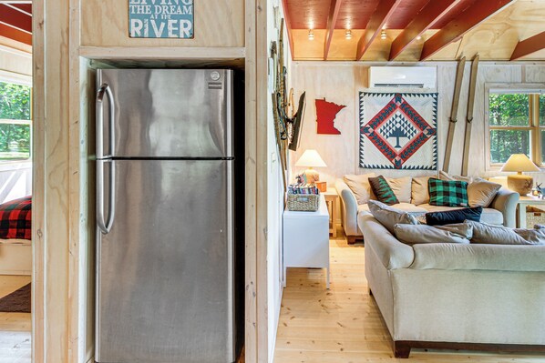 A modern kitchen with a stainless steel refrigerator, wooden flooring, and a cozy living area with a sofa and decorative pillows. - Riverside Retreat in Crosby: Pet Friendly! (Crosby)