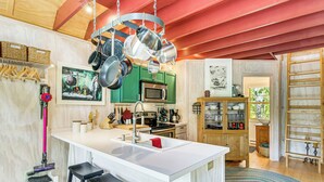 Uma cozinha moderna com ilha central, panelas de aço inoxidável, micro-ondas e armários verdes.