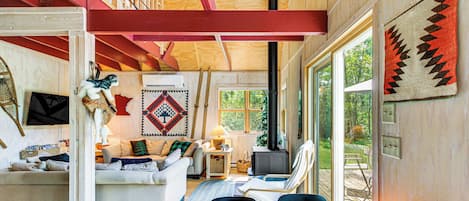 Interior acogedor de una cabaña con chimenea, sofá, mesa de comedor y un ventanal con vistas al exterior.