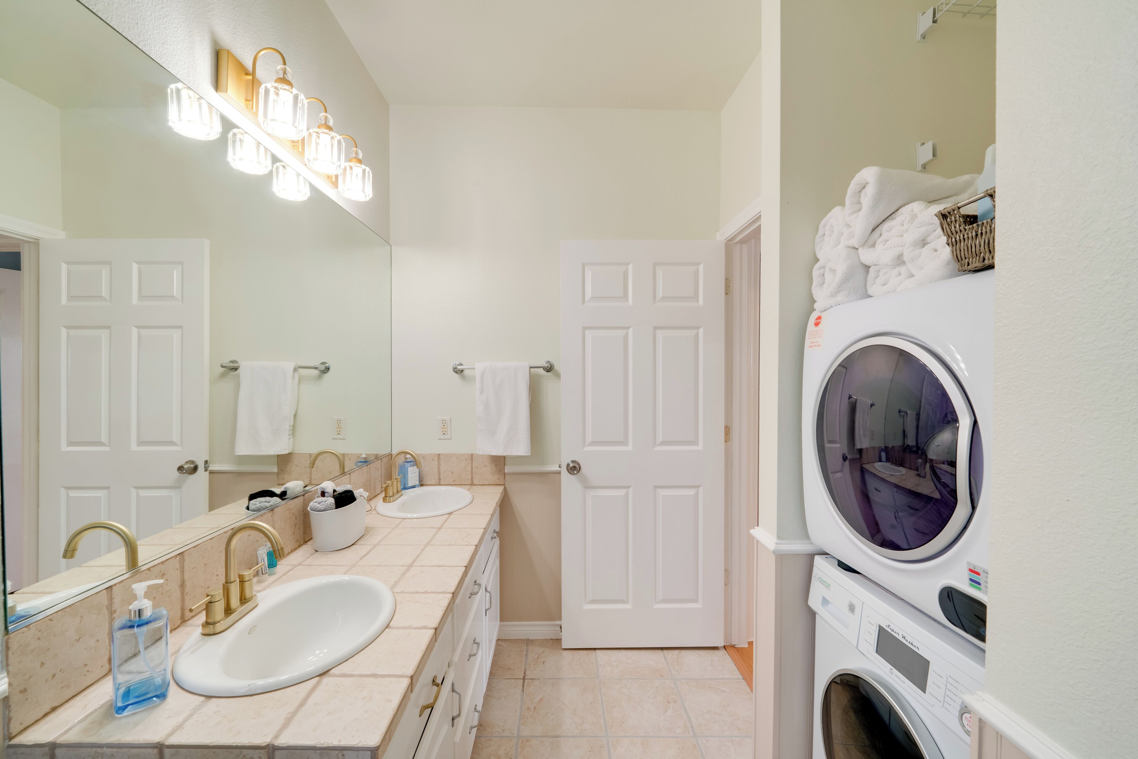 A bathroom with a sink, mirror, towel rack, and a stacked washer and dryer.