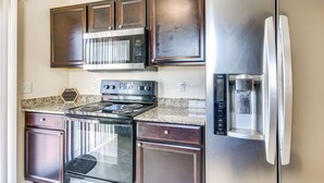Une cuisine dotée de meubles en bois foncé, d’appareils électroménagers en acier inoxydable, notamment un réfrigérateur, un four à micro-ondes et une cuisinière, et d’un comptoir en granit.