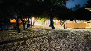 En strand med sand, palmer og en bygning i baggrunden.