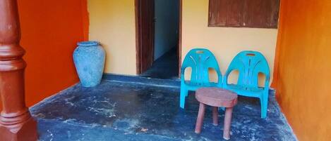 Un petit espace extérieur clos, doté d’un sol carrelé, d’une porte en bois et de deux chaises en plastique bleues.