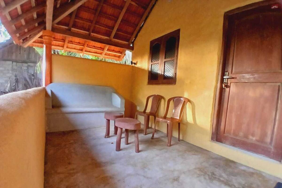 A room with a concrete floor, a wooden door, and a window with a lattice design. There are two wooden chairs and a small table.