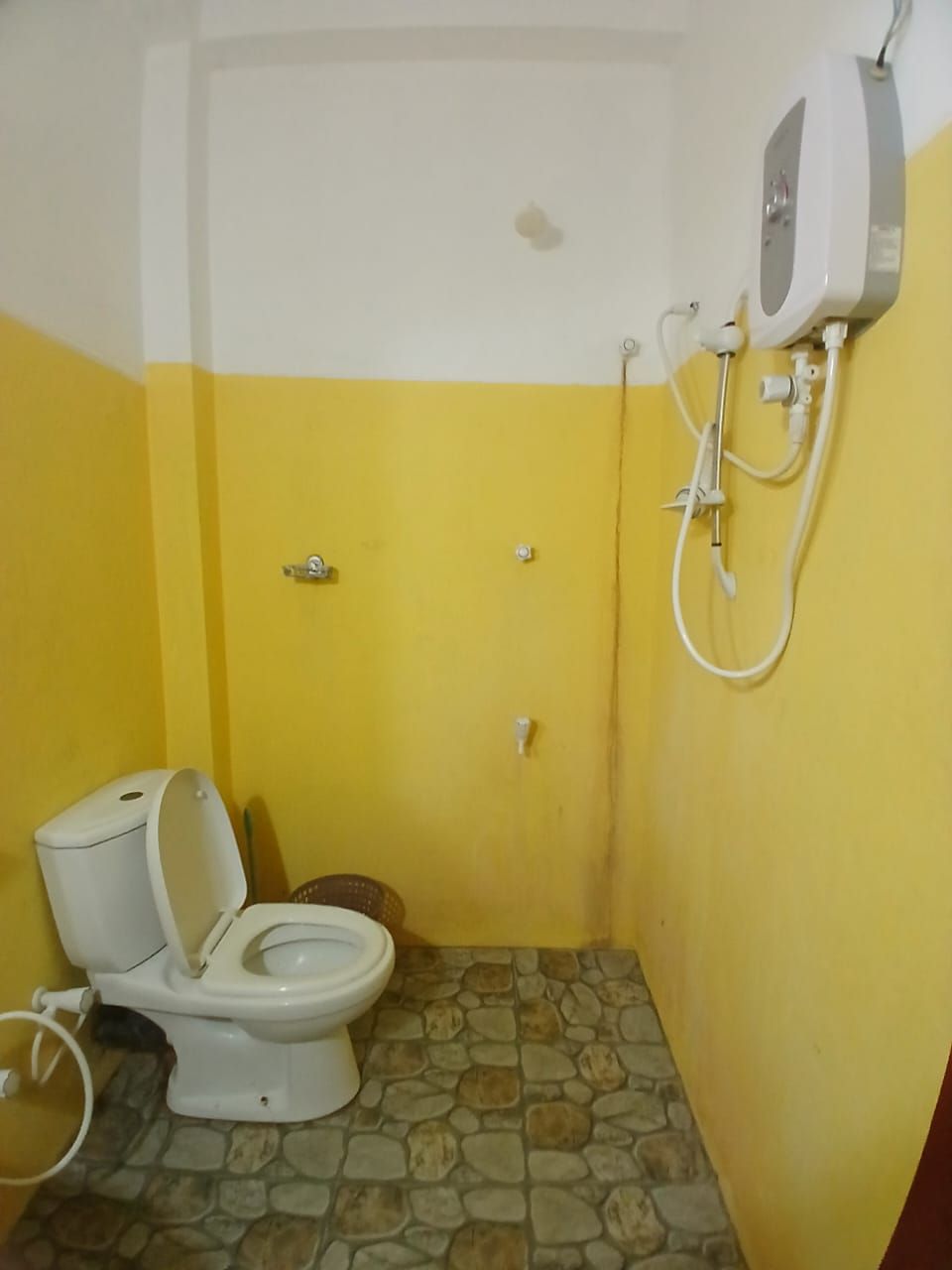 A small bathroom with a toilet, a shower unit, and a stone-tiled floor.