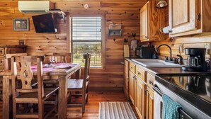 A wooden cabin interior with a dining area, kitchen, and a window with blinds.