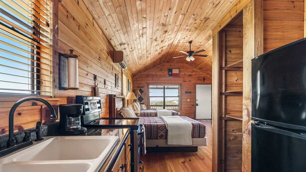 A cabin interior with a kitchen, a dining area, a bedroom, and a large window.