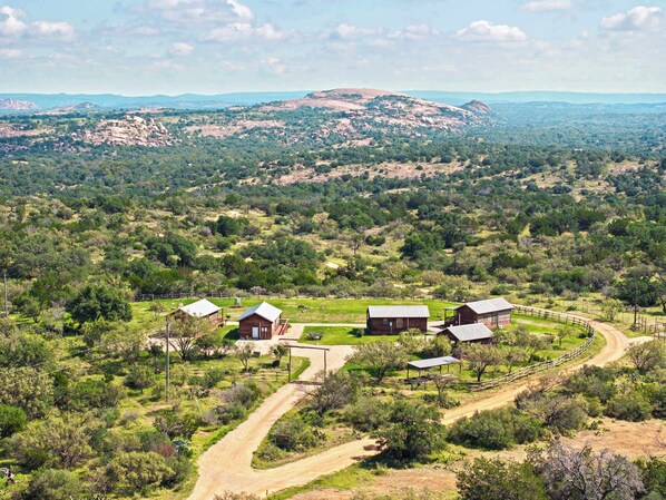 A rural property with multiple cabins, a dirt road, and a hilly landscape in the background.