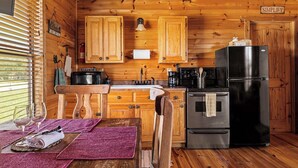 Cocina tipo cabaña con paredes de madera, un lavamanos, una estufa, un refrigerador y una ventana con persianas.
