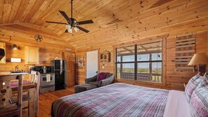 Una habitación tipo cabaña de madera con cama, una silla, un escritorio, un refrigerador y una ventana con persianas.
