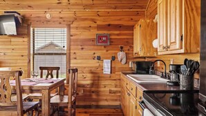 Interior de una cabaña de madera con comedor, cocina y una ventana con persianas.