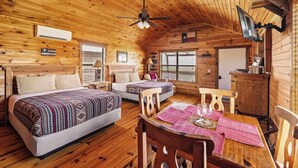 Una habitación tipo cabaña de madera con dos camas, una mesa de comedor y un ventilador de techo.