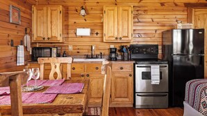 Interior de una cabaña de madera con zona de cocina, que incluye un refrigerador, estufa, microondas y armarios de madera.