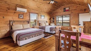A cabin-style room with two beds, a ceiling fan, wooden walls, and a view through the windows.