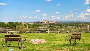 A grassy area with two wooden benches and a stone wall, overlooking a hilly landscape with a clear sky.