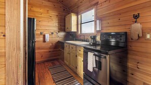 A compact kitchen with wooden walls, a stainless steel stove, a coffee maker, and a window with blinds.
