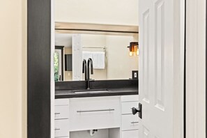 Une salle de bain moderne avec un plan de toilette noir, des meubles blancs, un grand miroir et une serviette accrochée au mur.