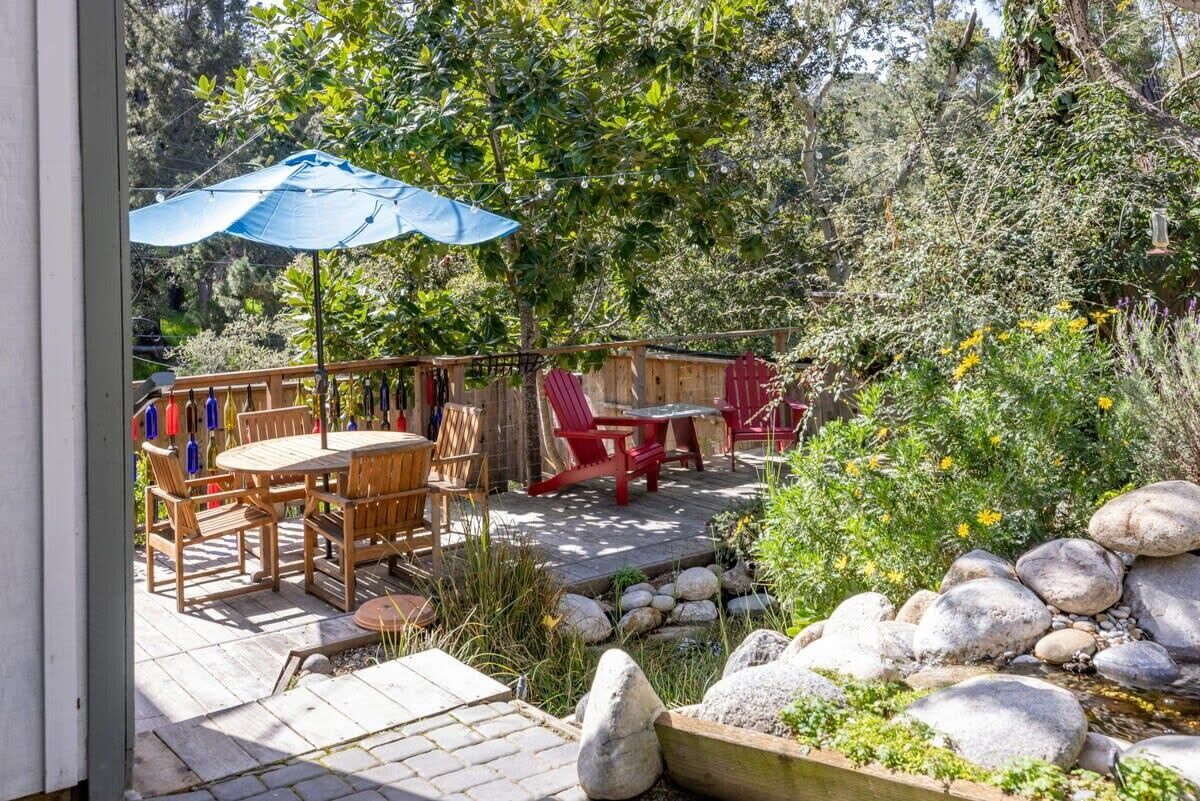 An outdoor patio with a wooden table and chairs, a blue umbrella, and a wooden deck.