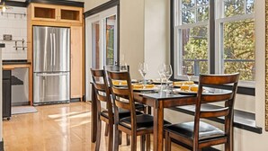 Una cocina moderna con un refrigerador de acero inoxidable integrado, armarios de madera y un comedor con una mesa dispuesta para cuatro.