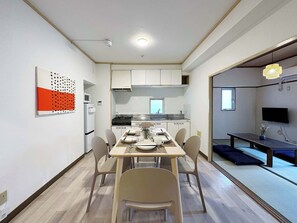 A modern kitchen with white cabinets, a dining area with a table set for four, and a TV mounted on the wall. - Dai3kuboi 305 (Hiroshima)