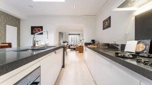 A modern kitchen with a central island, a dining area with a sofa, and a view into the living room. - Maison La Roussette - in the heart of Nieuwpoort (Nieuwpoort)