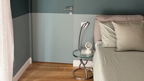 Een kamer met een deur, een glazen tafel met een lamp, een bed met kussens en een houten vloer.