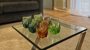 Een woonkamer met een glazen salontafel, een grijze bank, kunstwerken in lijsten en een radiator.