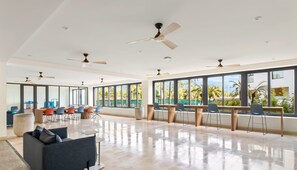 A spacious room with large windows, ceiling fans, and a mix of seating arrangements including chairs and a sofa.