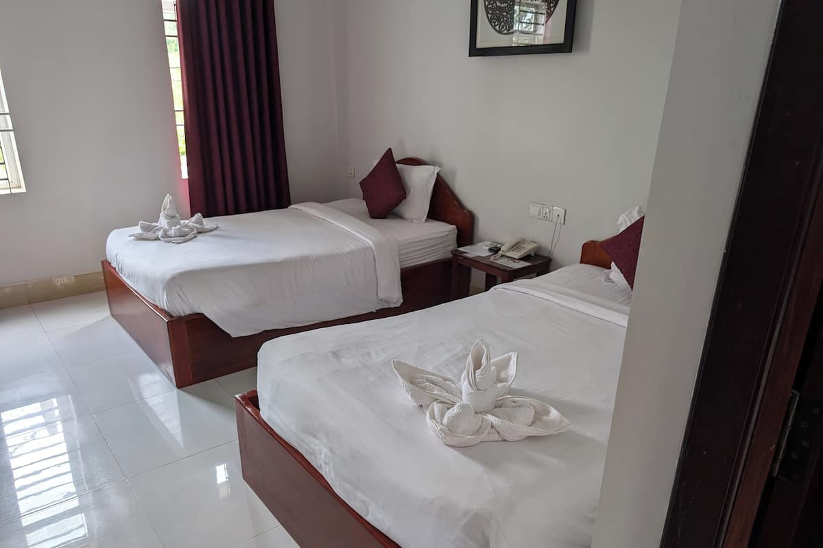 A hotel room with two beds, each with white linens and towels. There is a nightstand with a phone and a small table with a lamp.